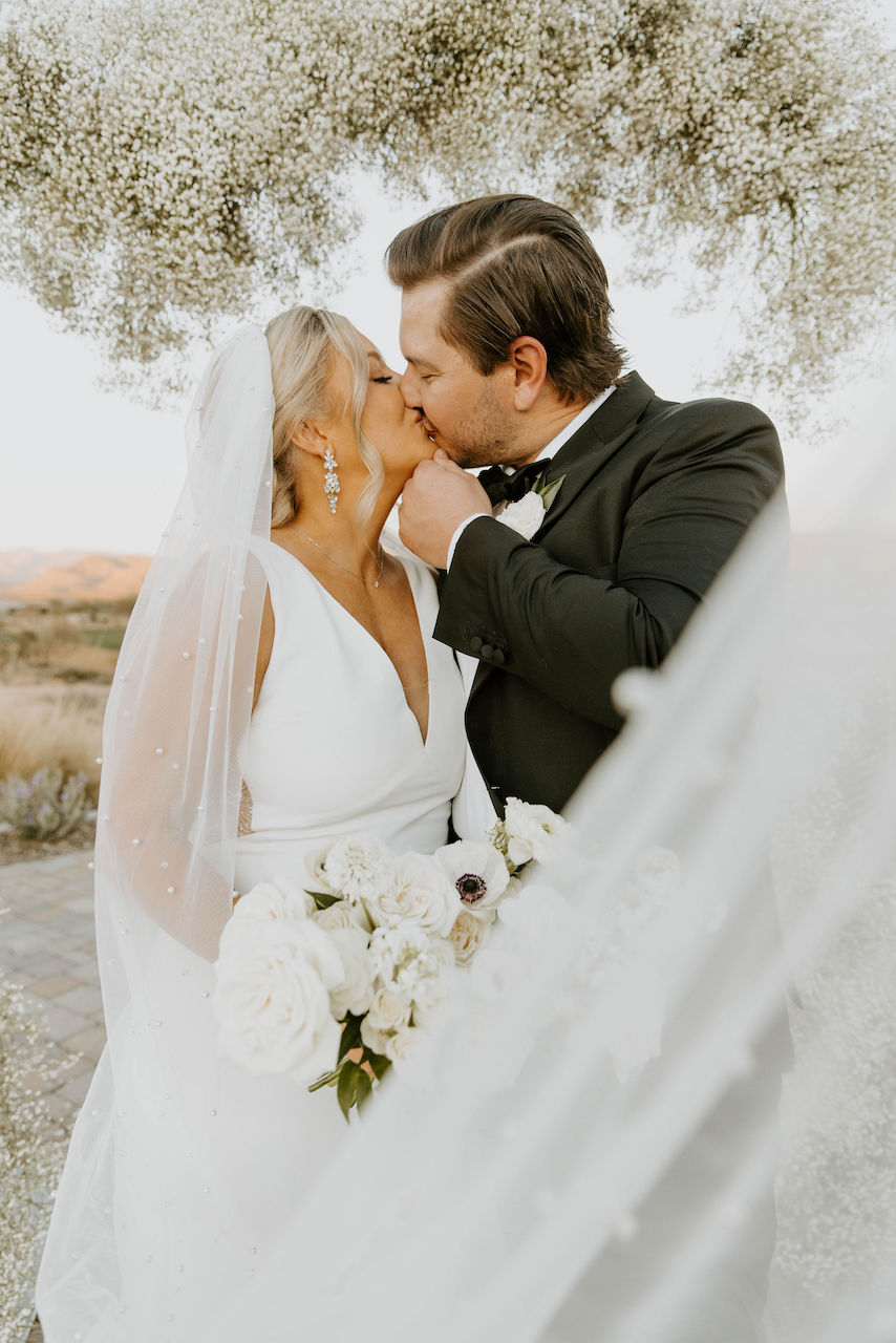 Bride and groom kissing in front of wedding ceremony baby's breath arch.