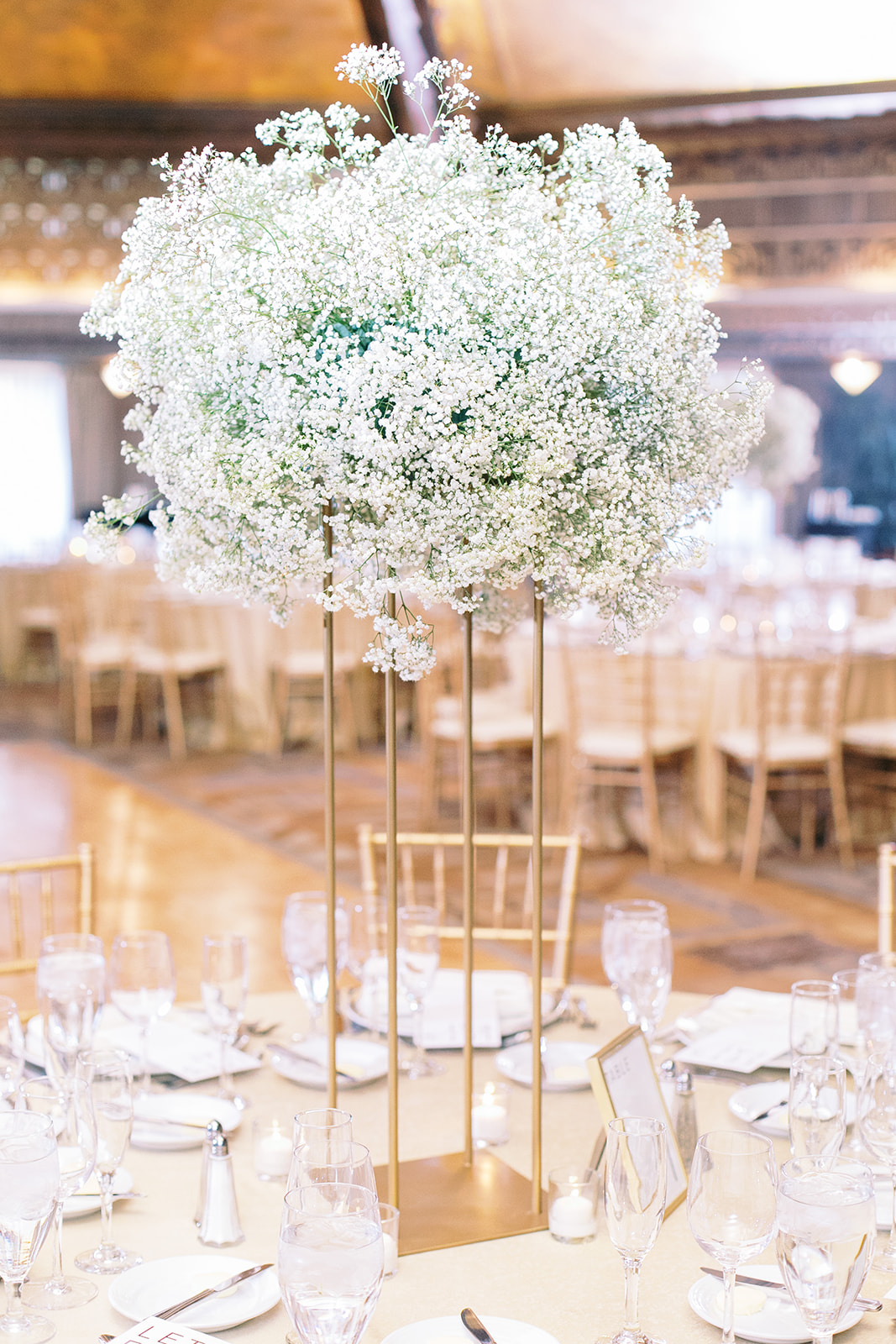 Tall wedding reception centerpiece on gold stand of baby's breath.