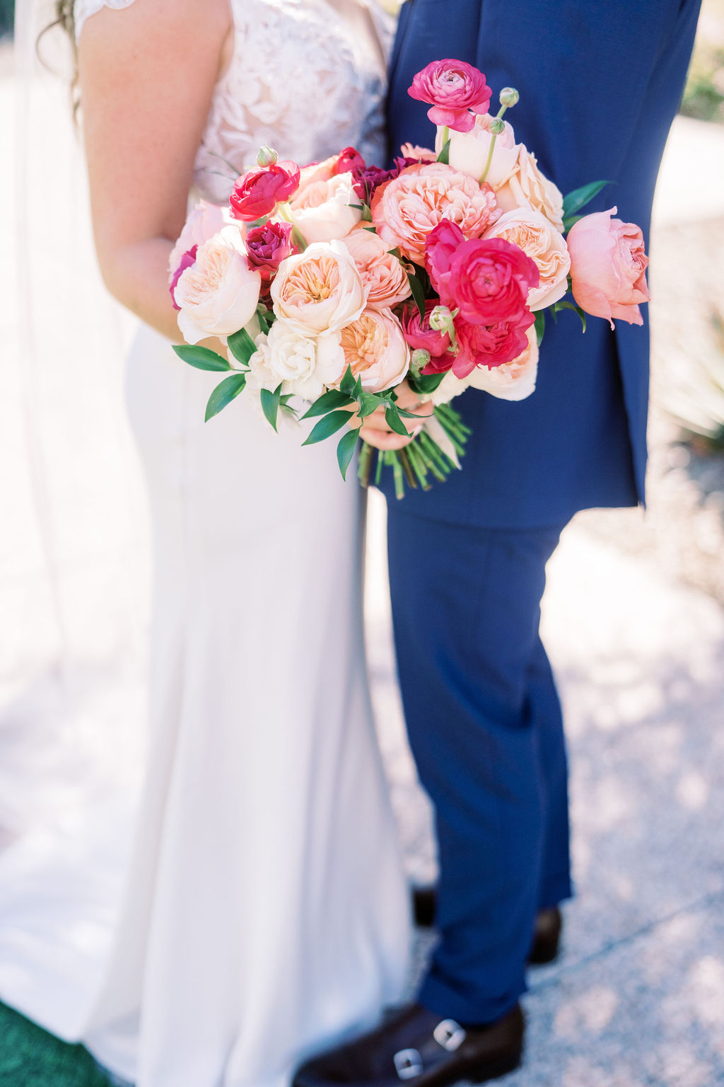 Bridal bouquet of pink and peach flowers including ranunculus and roses.