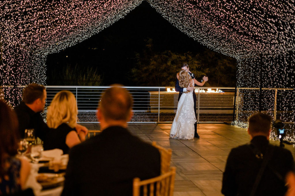 Bride and groom dancing outside at reception under draped lights.