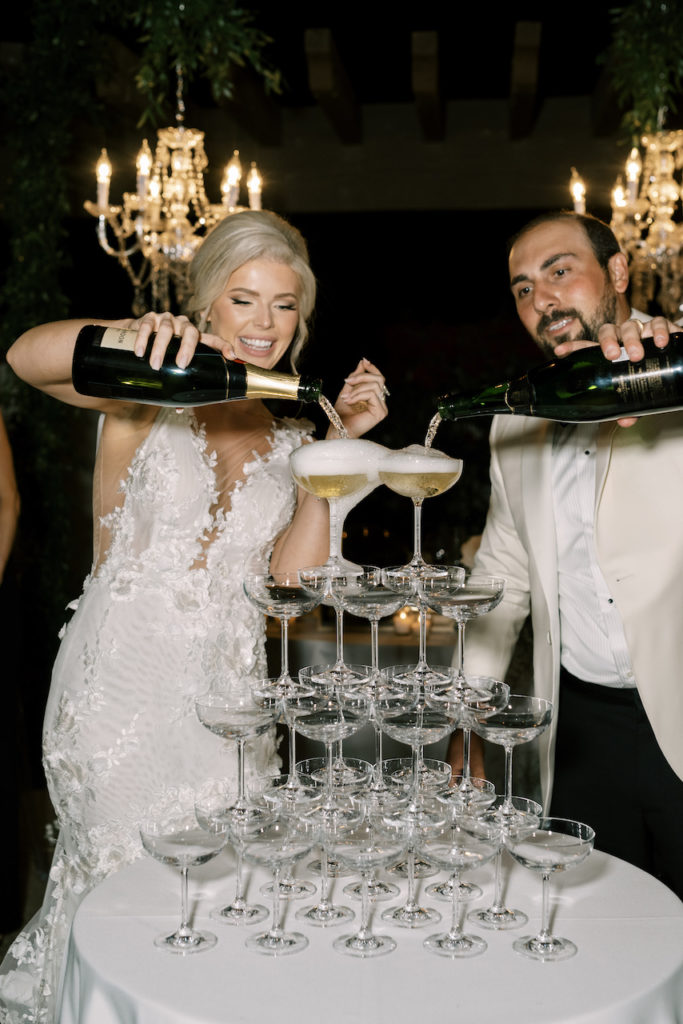 Bride and groom pouring champagne over glasses in tower.