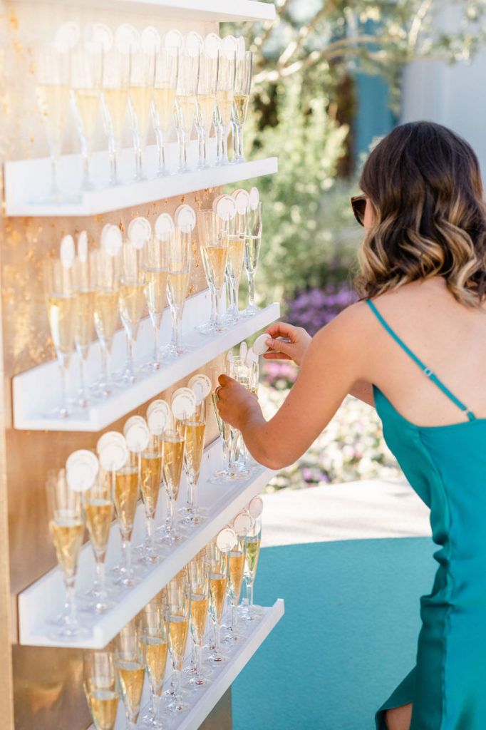 Placing of guest champagne glasses on shelved guest escort board at wedding.