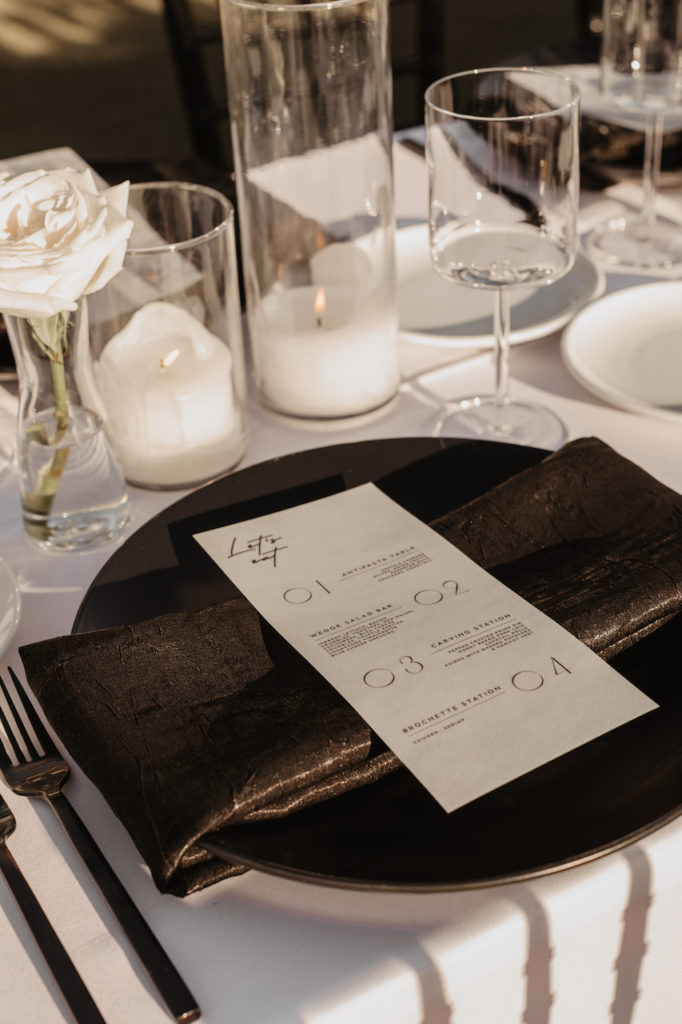 Wedding reception place setting with black plate, candles, and white floral bud vase.