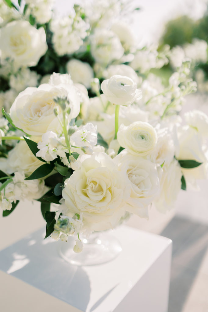 Wedding ceremony floral arrangement of white flowers and greenery in clear glass vase.