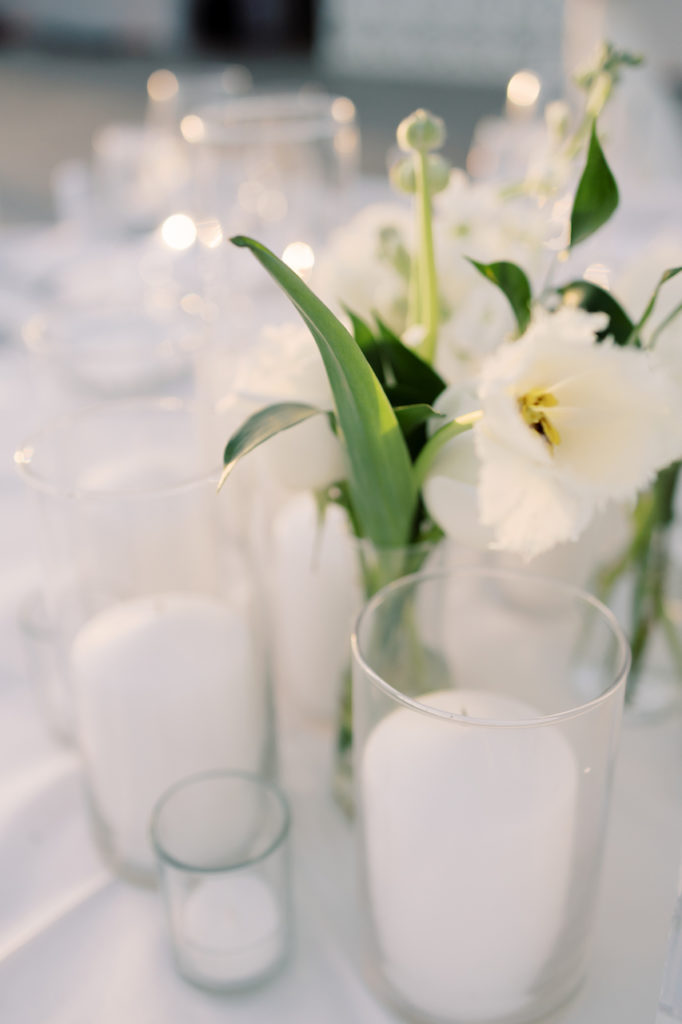 Pillar candles in vases with bud vase of white flower.
