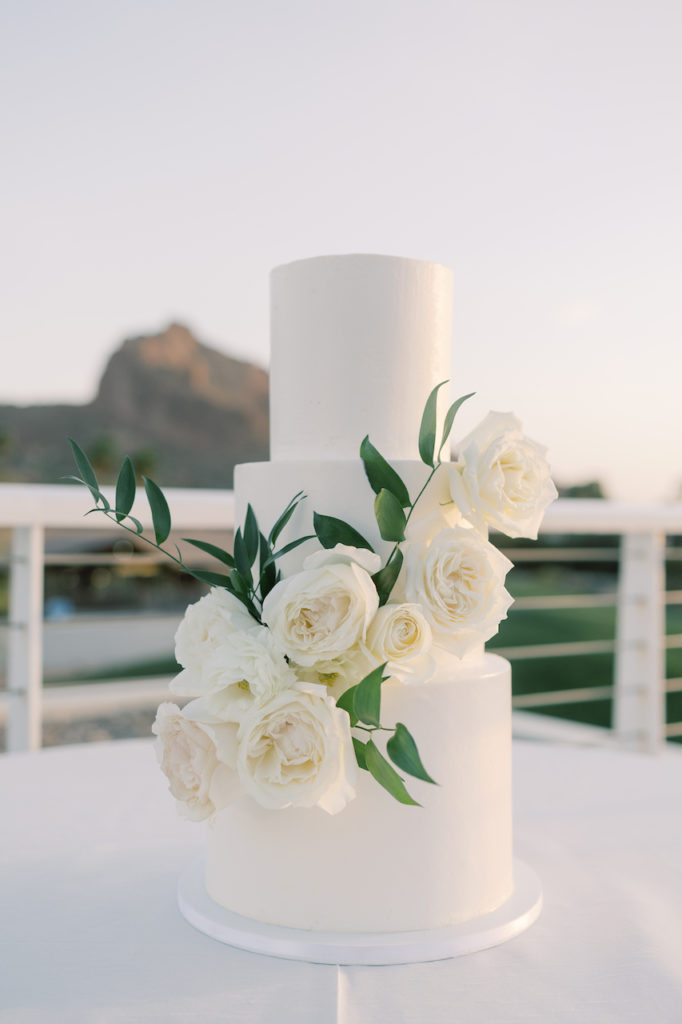 Three tiered white wedding cake with white roses and greenery.