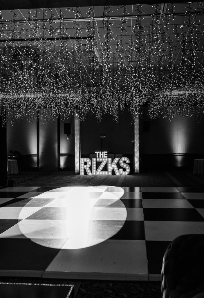 Wedding reception dance floor with handing lights and couple's last name in lights with black and white checkered dance floor.