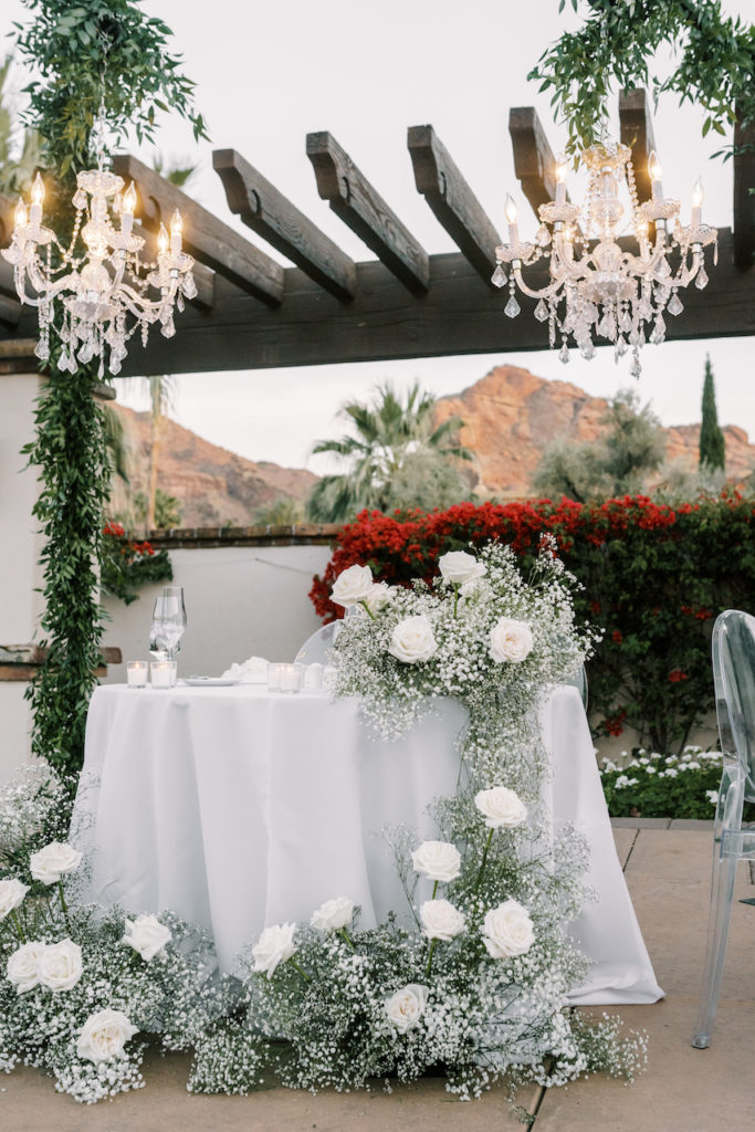 Sweetheart table with handing overhead chandeliers and cascading baby's breath and white roses garland.