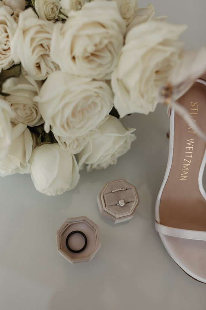 Wedding details of rings and bridal shoes with white roses.