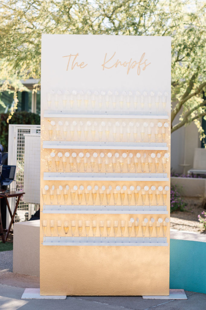 Custom guest escort board of gold with shelves filled with champagne glasses.