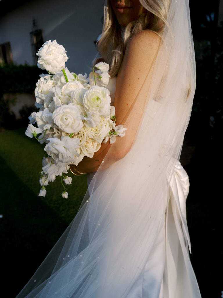 Bride holding and looking down at elegant white flowers bouquet.