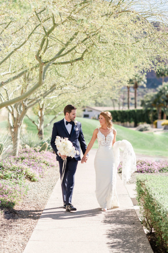 Bride and groom holding hands walking on an outdoor path.