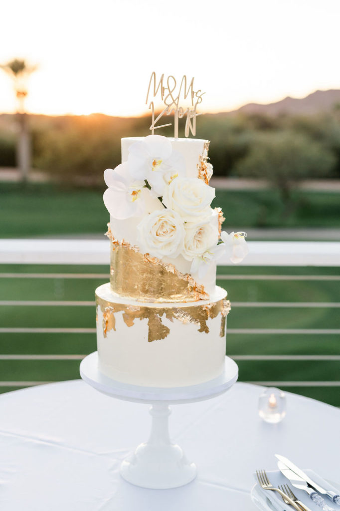 Three tiered wedding cake with gold flake and white floral.