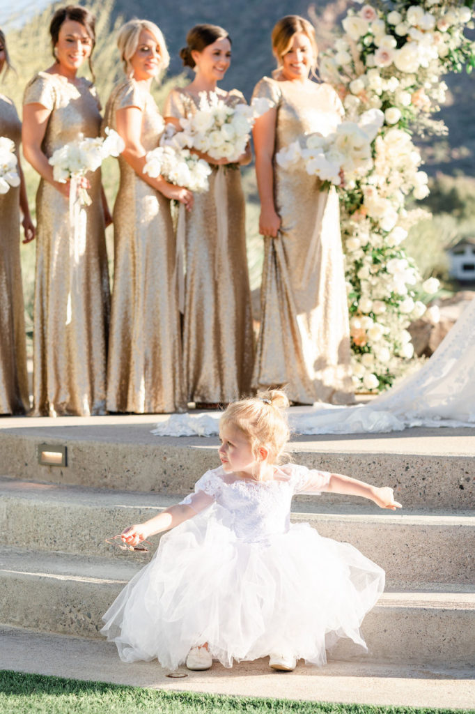 Flower girl sitting on steps of outdoor wedding ceremony.