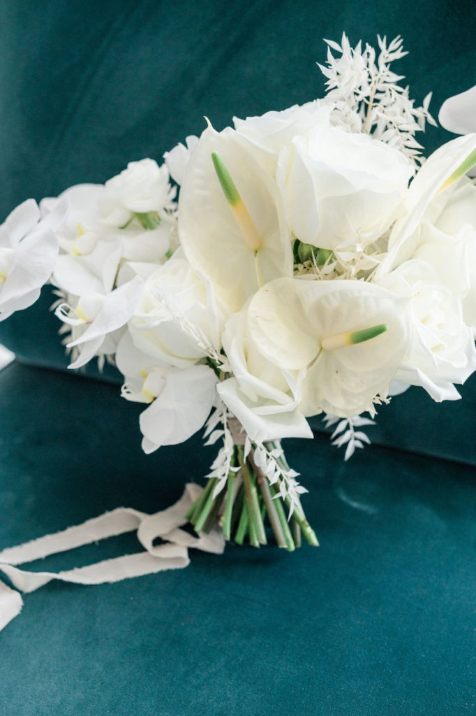 Bridal bouquet of white flowers including bleached Italian ruscus, anthurium, and orchids.