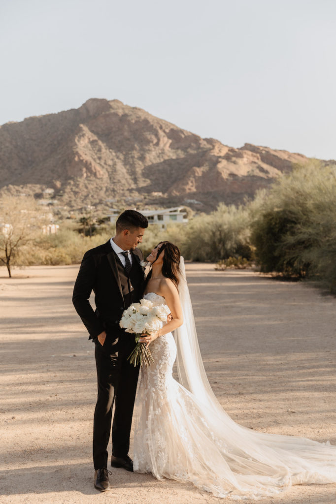 Bride and groom smiling and looking at each other in desert setting at El Chorro with desert mountain setting behind them.