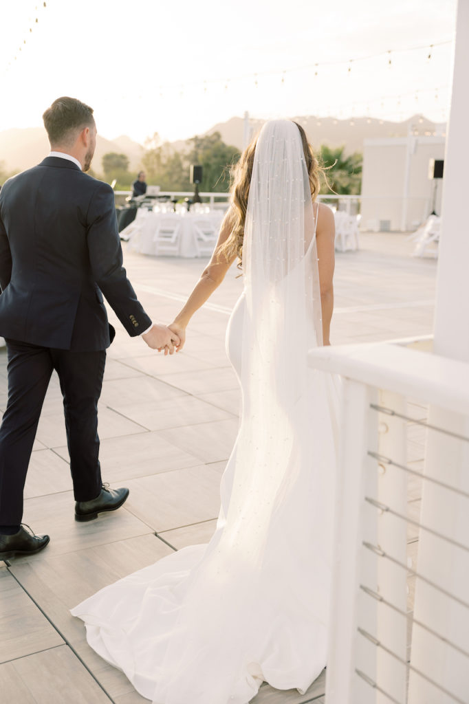 Bride and groom walking away onto deck holding hands.