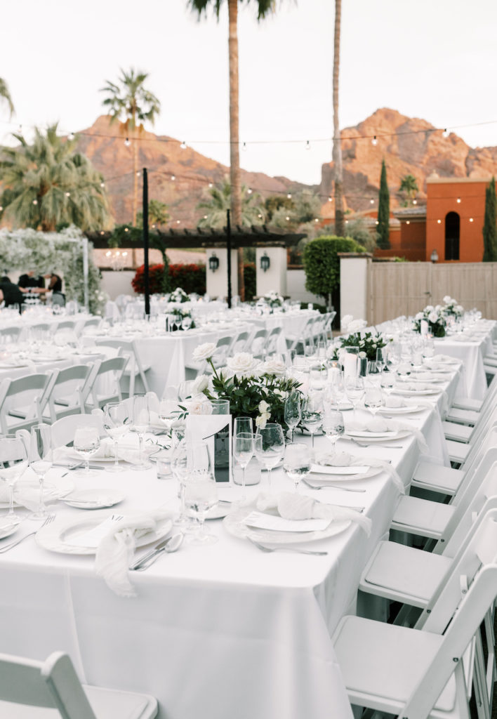 Outdoor wedding reception of long white tables with white place settings at Omni Montelucia resort.