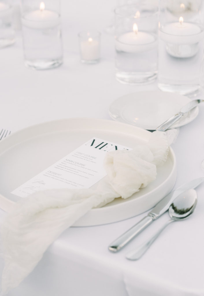 Floating white candles and white plates at wedding reception place setting.