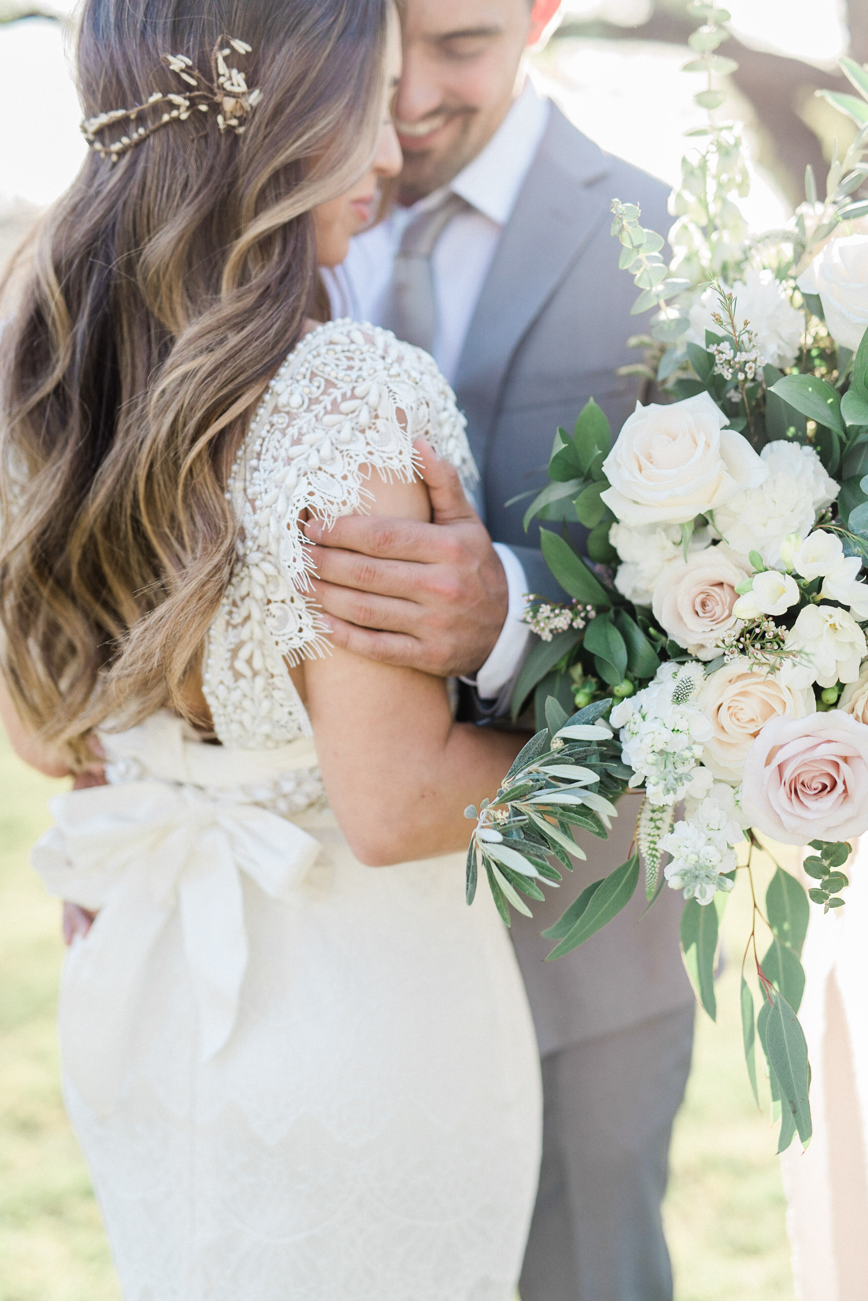 Bride and groom embracing, bride holding bouquet, both smiling.