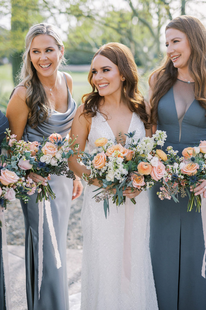 Bride with bridesmaids wearing slate blue dresses, all holding bouquets.