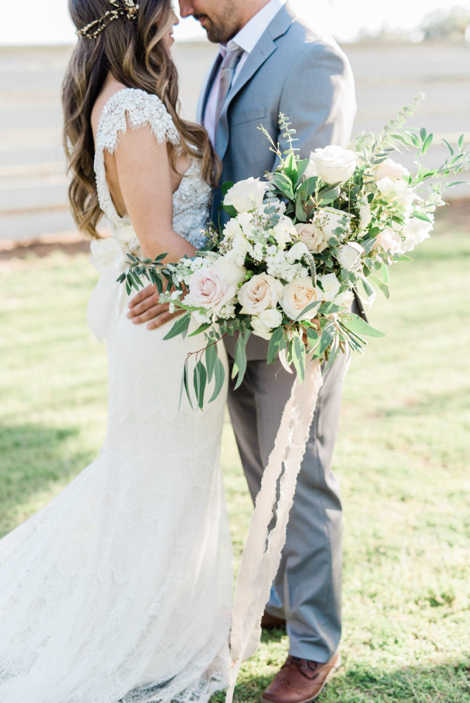 Bride and groom facing each other standing in grass yard, bride holding bouquet.