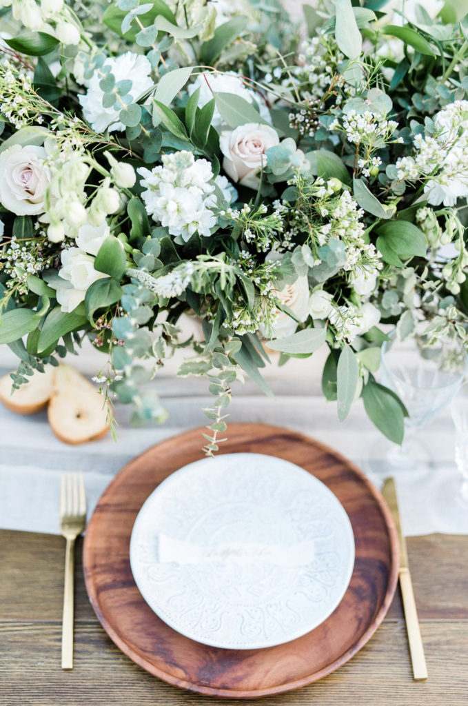 Place setting with floral centerpiece of white, light pink flowers and greenery.