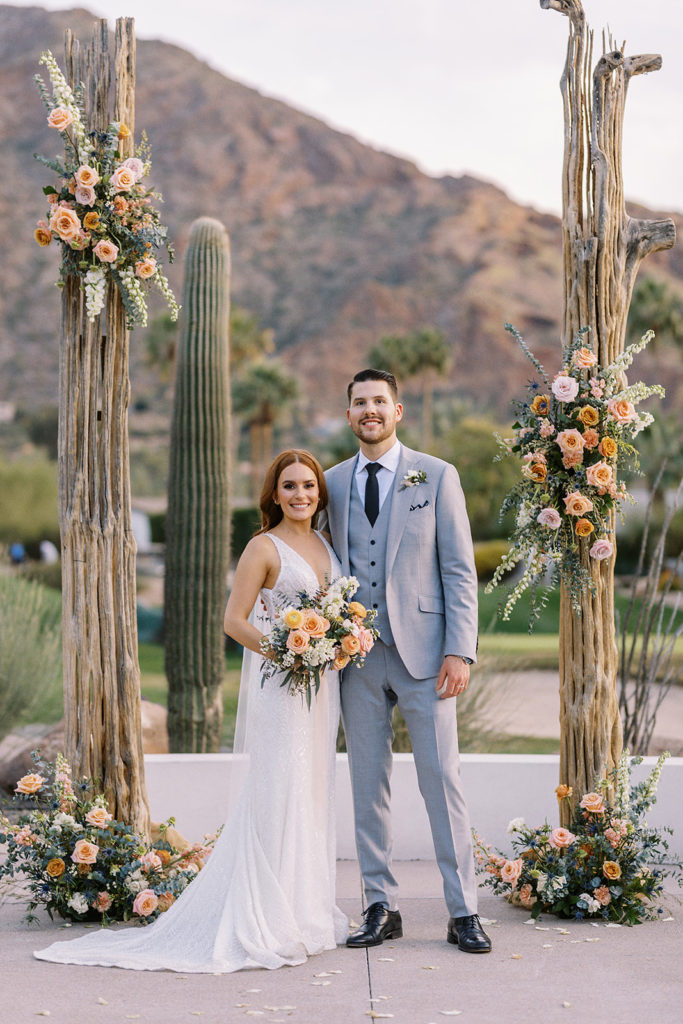 Bride and groom standing between saguaro ribs with floral installation design at Mountain Shadows wedding ceremony.