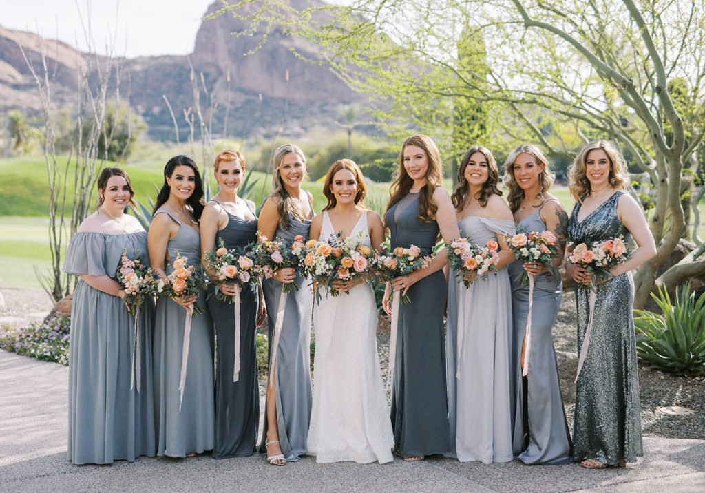 Bride standing in line with bridesmaids wearing slate gray dresses, all holding bouquets.