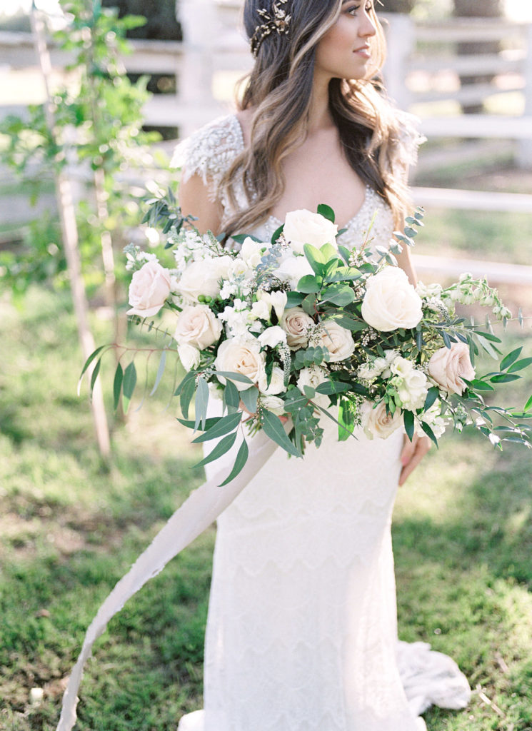 Bride holding white and light pink floral bouquet and greenery, looking off to side.