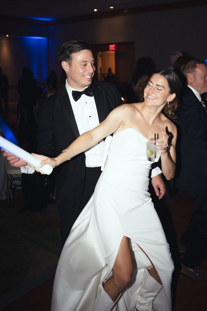Bride in wedding dress and white cowboy boots dancing with groom during wedding reception.