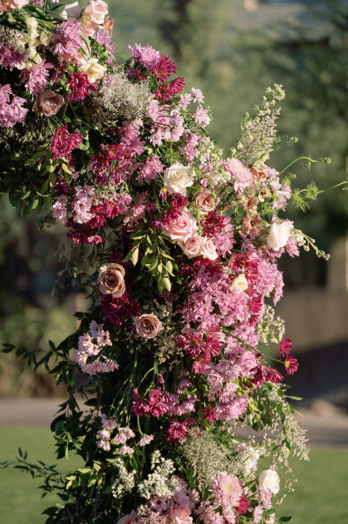 Close of details of floral on wedding ceremony arch filled with greenery, pink and mauve flowers.