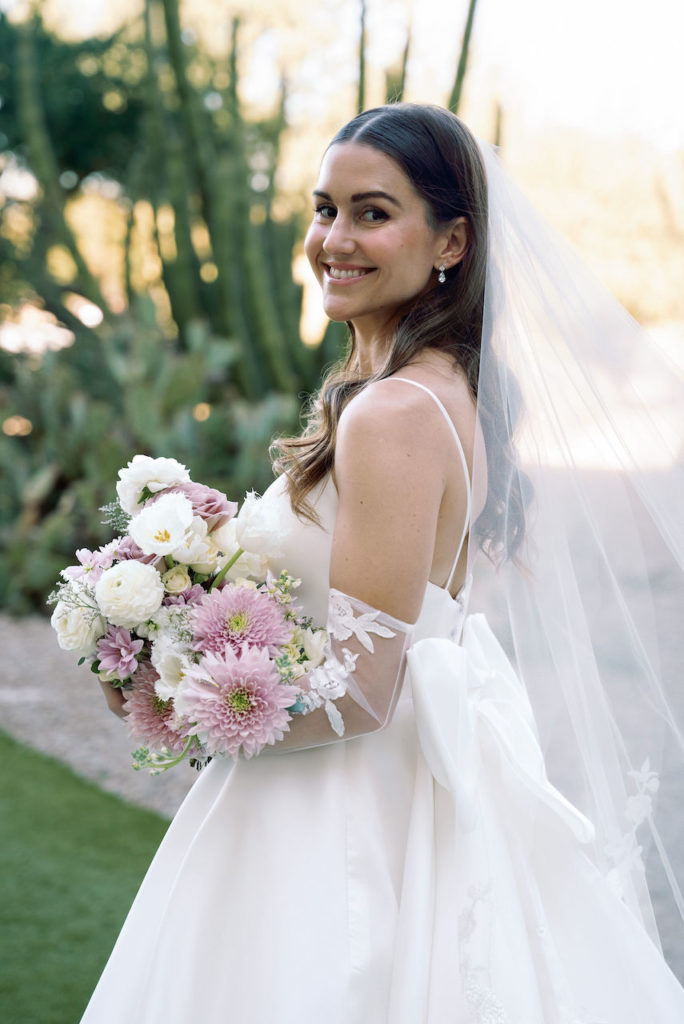 Bride smiling over shoulder wearing wedding dress and holding bouquet.