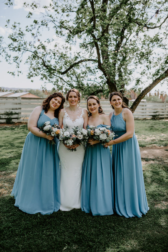 Bride standing with bridesmaids in blue dresses, holding bouquets.