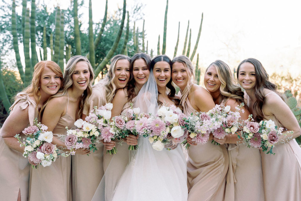 Bride with bridesmaids smiling and all holding bouquets with a desert background behind them.