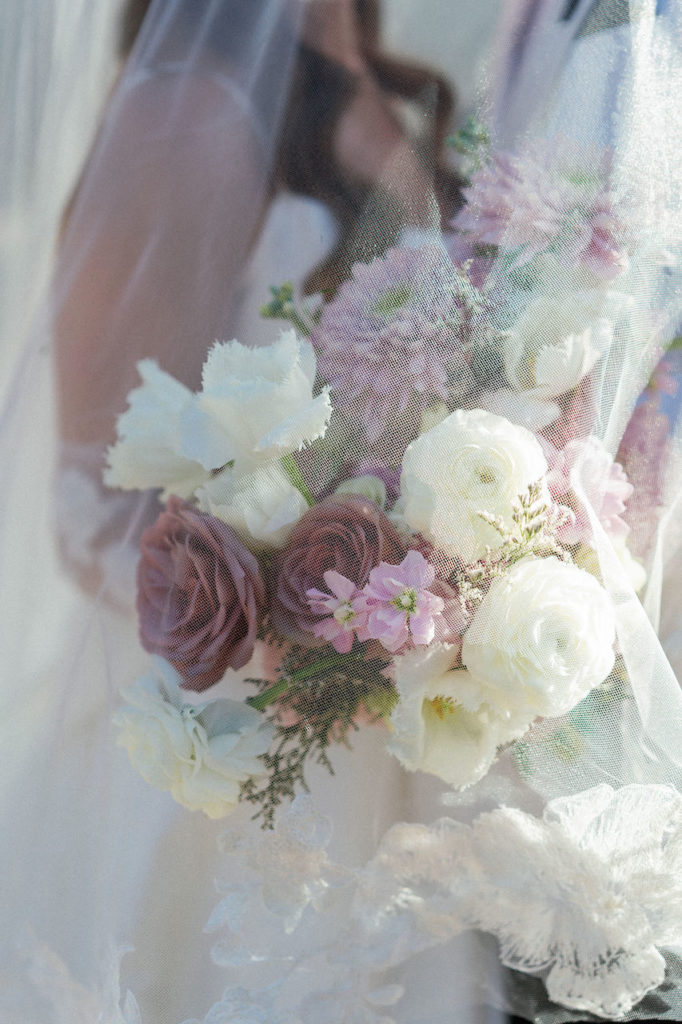 Bridal bouquet held by bride of white, mauve, and pink flowers.
