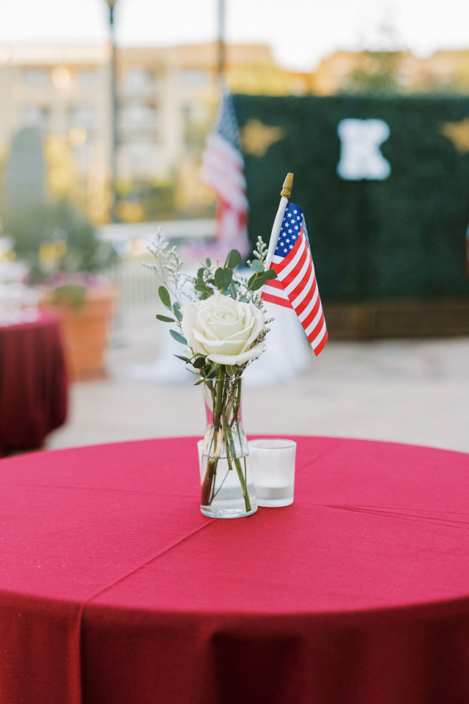 Cocktail hour high boy table with white rose, greenery, and American flag.