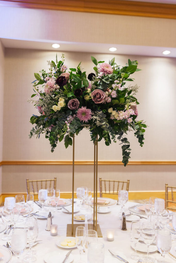 Tall reception centerpiece of brass with floral and greenery on top.