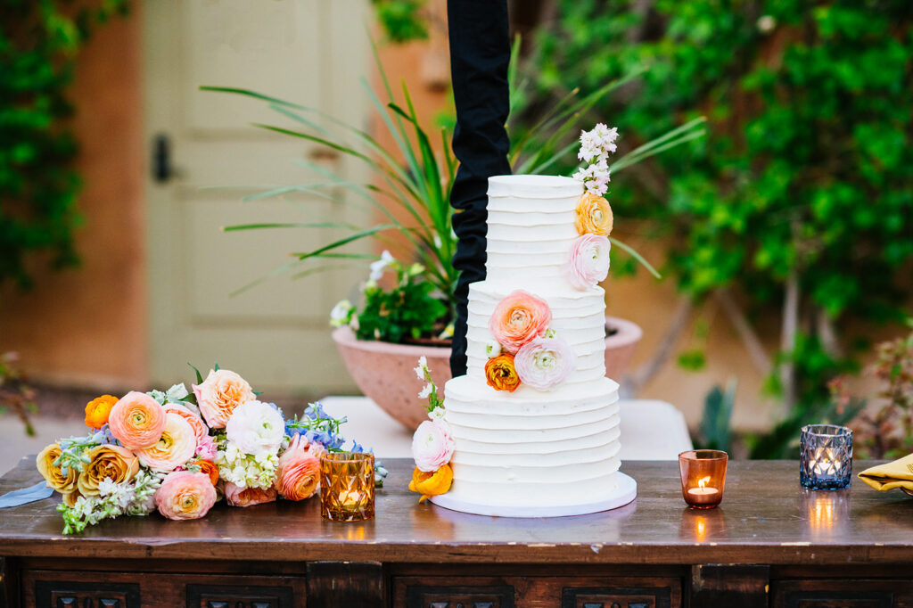 Three tiered white wedding cake with flowers and votives.