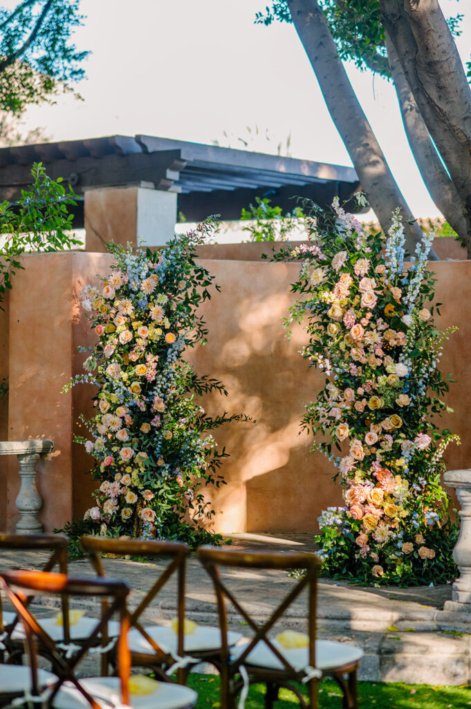 Lush custom wedding ceremony floral columns of pink, peach, yellow, and blue flowers and greenery.
