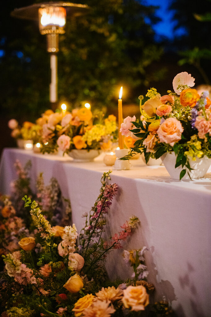 Evening outdoor wedding reception with lush floral of pink, orange, and blue.
