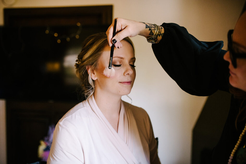 Bride getting makeup applied by makeup artist.