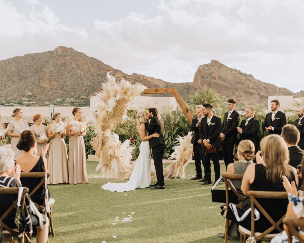 Bride and groom kissing in front of hexagon arch at outdoor wedding ceremony at Camelback Inn.