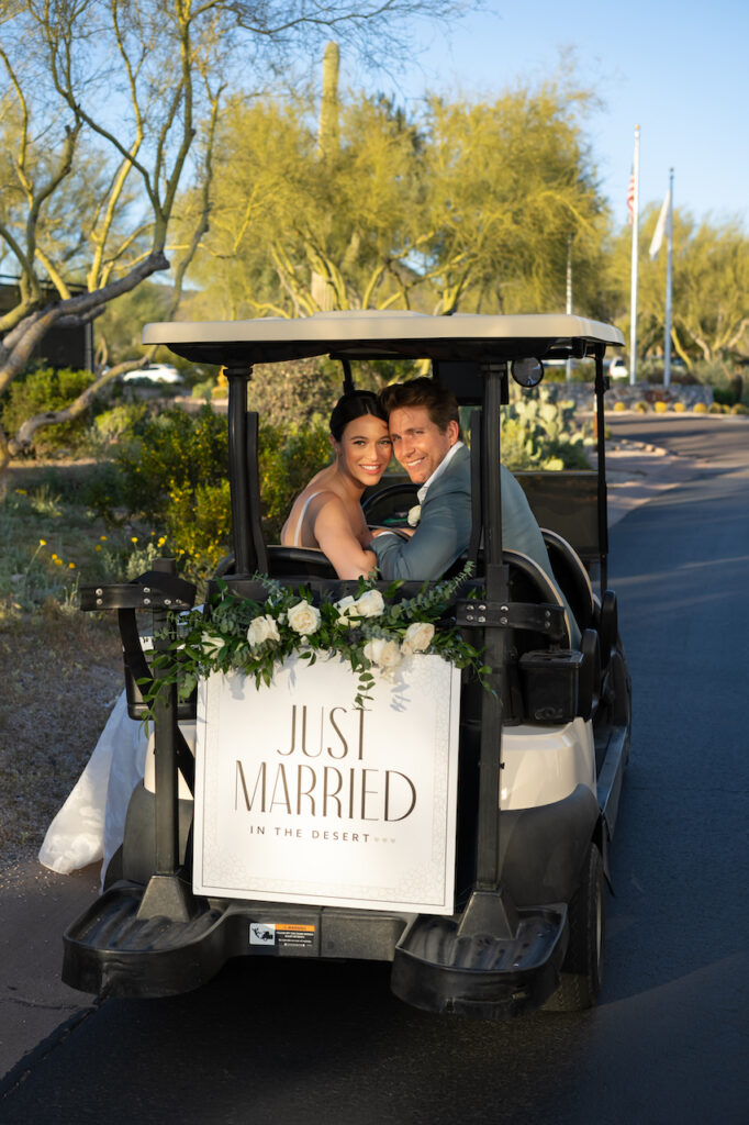 Bride and groom in golf cart that has Just Married sign on back.