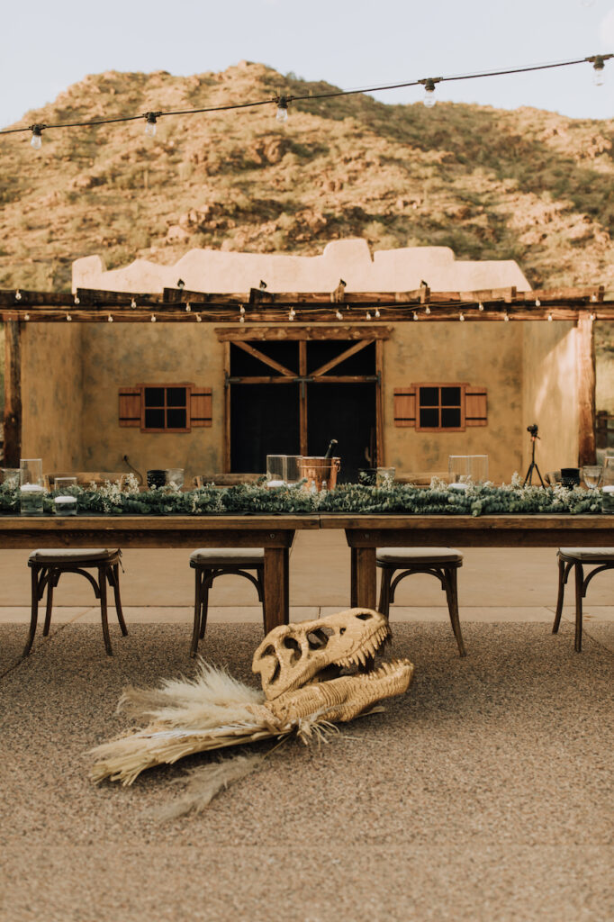 Camelback Inn outdoor wedding reception head table with layered greenery, candles and dinosaur skull placed on ground in front with pampas.