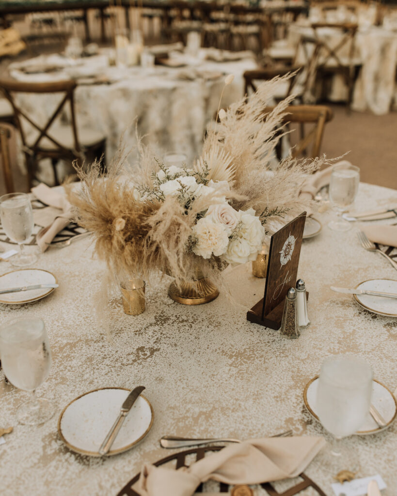 Low wedding reception centerpiece of white floral and dried elements.