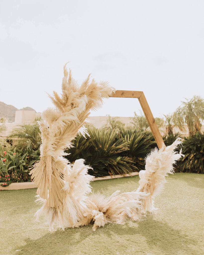 Hexagon wedding ceremony arch made of wood and decorated with dried pampas and palms.