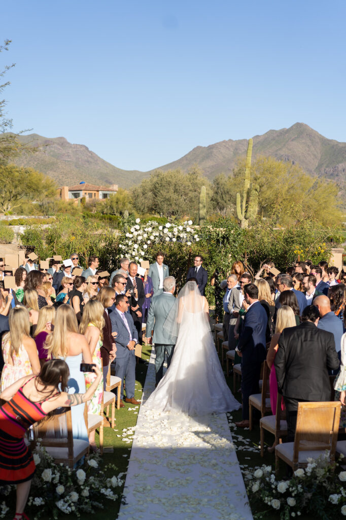 Bride being escorted down wedding ceremony aisle at outdoor ceremony at DC Ranch with desert landscape background setting.