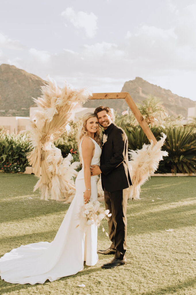 Bride and groom resting heads together in front of pampas decorated hexagon arch at Camelback Inn.
