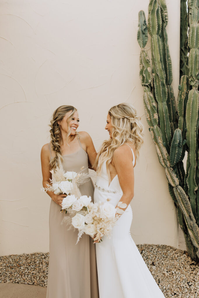Bride smiling with bridesmaid standing next to each other, both holding bouquets.